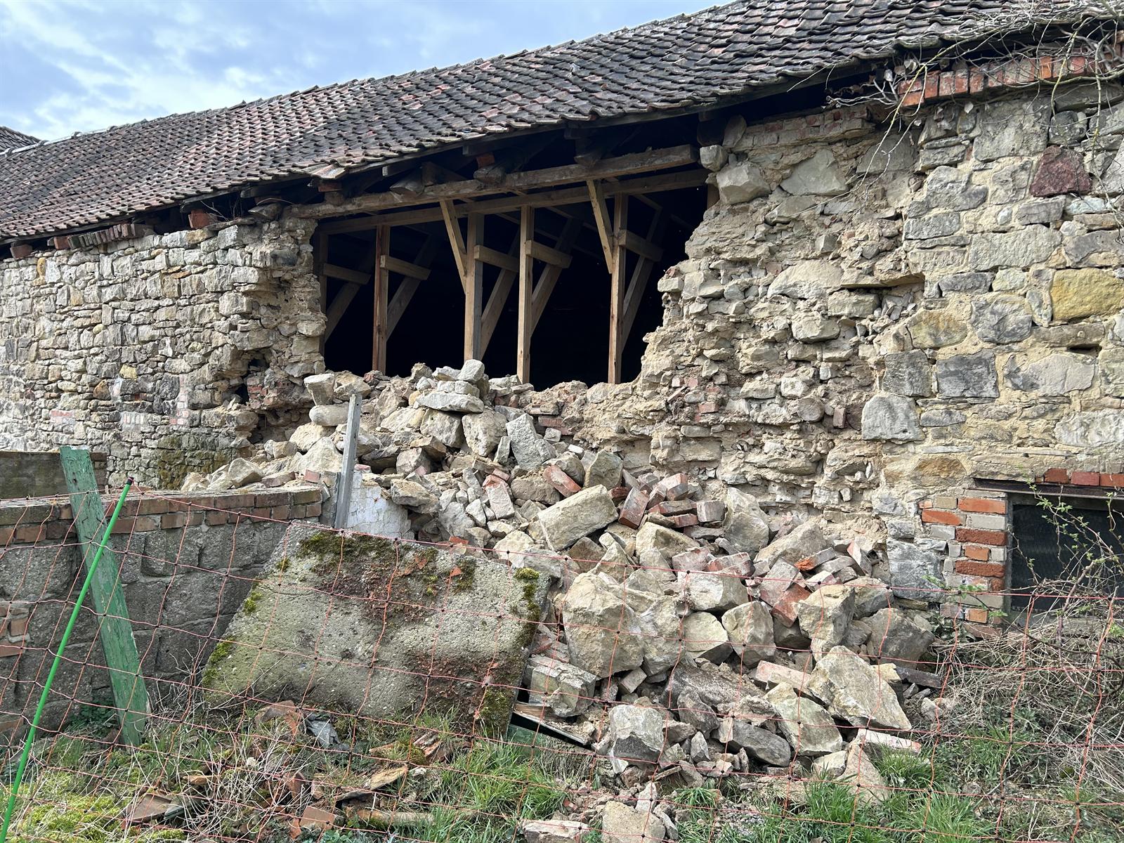 Eingestürzte Natursteinwand einer Scheune, das Mauerwerk liegt als Haufen davor