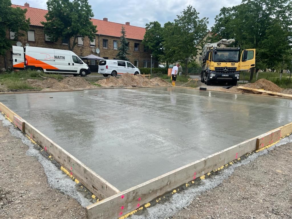 Frisch betonierte und abgezogene Bodenplatte in der Schalung, dahinter Betonpumpe und Dreinath-Fahrzeuge