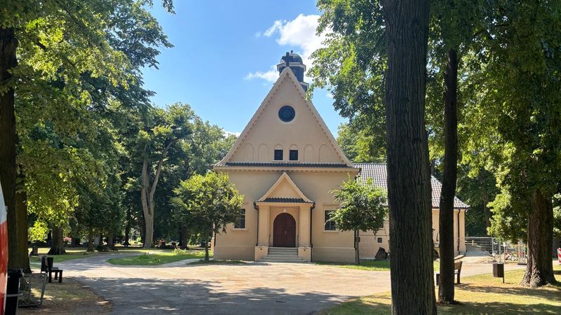 Sanierte Kapelle mit hellem Putz, umgeben von alten Bäumen