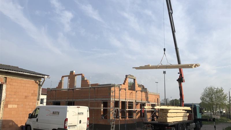 Autokran hebt Dachbinder auf einen Rohbau