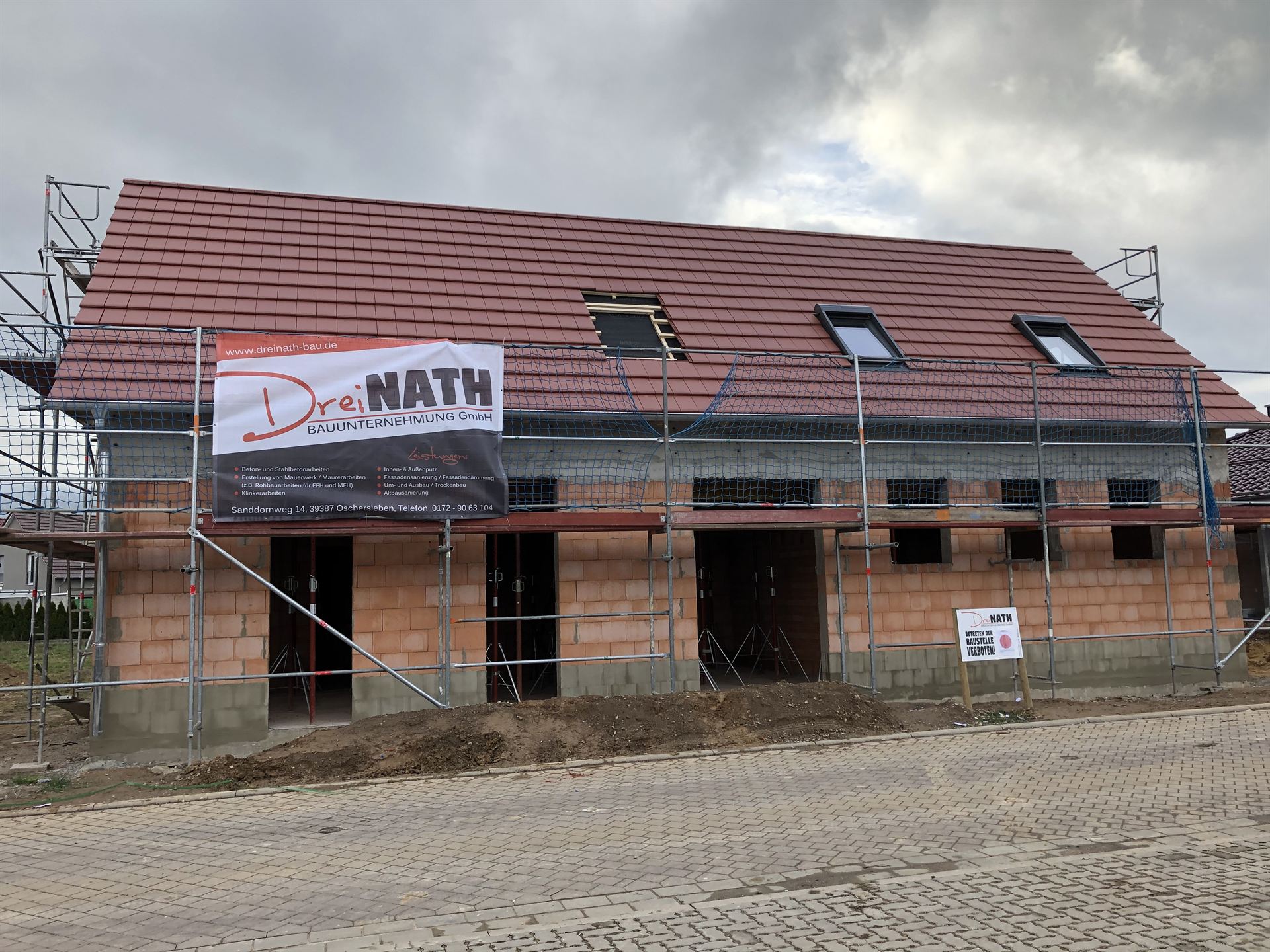 Rohbau eines Einfamilienhauses aus Ziegelmauerwerk mit Gerüst und Dreinath-Banner