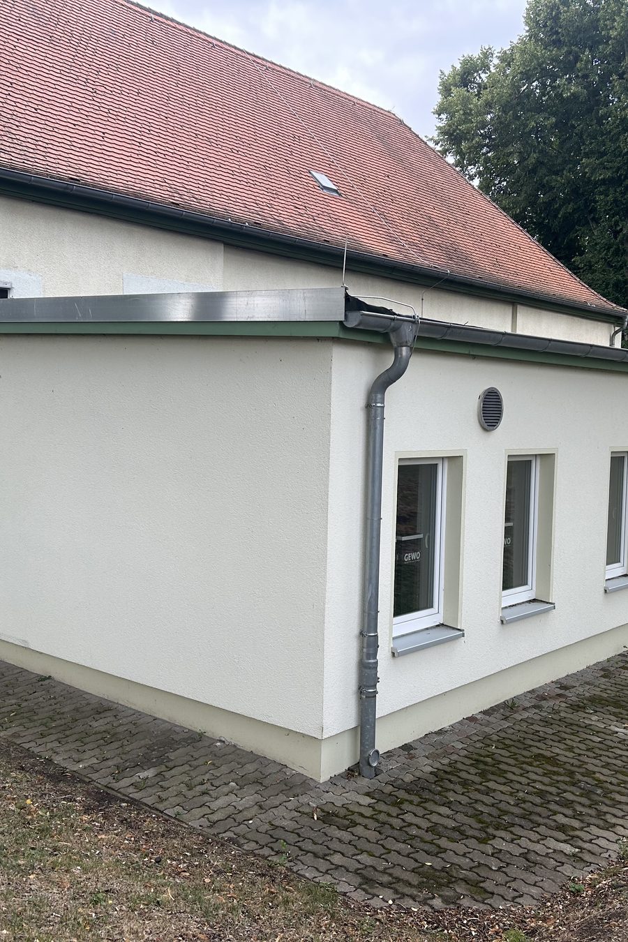 Derselbe Anbau nach der Sanierung mit neuem Putz und gepflastertem Streifen